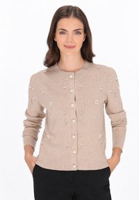 Beige ribbad kavaj med rund halsringning, prydd med dekorativa kulor och blommönster, med knappfront och långa ärmar.