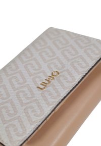 Portafoglio color crema con motivo geometrico a rilievo, logo in metallo dorato e base in pelle beige liscia. Forma rettangolare compatta.