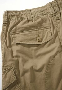Pantalones cortos de carga beige con una cinturilla elástica, que incluyen un bolsillo trasero con botón y un bolsillo lateral. Material de algodón suave con una textura sutil.