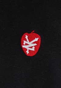 Crni materijal s crvenom izvezenom jabukom u središtu, koja ima bijeli uzorak. Jabuka ima mali stabljiku i teksturirane detalje.