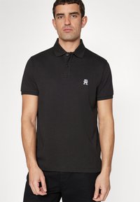Polo nero in cotone, con colletto a tre bottoni e logo bianco. Maniche corte con una vestibilità classica e una texture liscia.