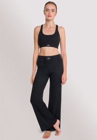 Ensemble de brassière de sport noire côtelée et de pantalon à jambes larges. Tissu texturé avec un haut ajusté et une taille élastiquée à cordon de serrage. Pas de motifs ni de logos visibles.