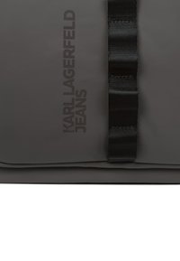 Μαύρη τσάντα με ματ φινίρισμα, με επίπεδο σχεδιασμό και πλεχτό μαύρο λουρί. "Karl Lagerfeld Jeans" εκτυπωμένο σε μαύρο κείμενο στο πλάι.