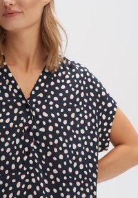 Kurze Bluse in Marineblau mit einem weißen und rosa Punktenmuster, ausgestattet mit einer Knopfleiste und einem lockeren Schnitt. Glatte Stofftextur.