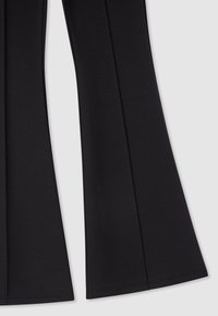 Pantaloni neri svasati realizzati in tessuto elasticizzato, caratterizzati da una texture liscia e cuciture pulite con un leggero splendore.