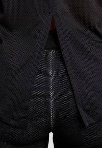 Svart atletisk outfit med en mesh topp med slits bak och tajta shorts med texturerad design och sömlös konstruktion.