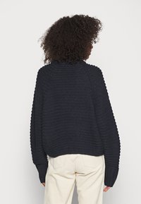 Marinblå stickad tröja med ribbad textur, raglanärmar och hög halsringning. Utrustad med långa, åtsittande muddar och en kortad nederkant.