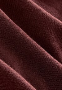 Tejido de punto burdeos con una textura suave, que presenta un canalé horizontal y un acabado liso. Los hilos están tejidos de manera ajustada y son ligeramente peludos.