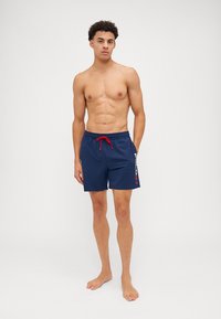 Shorts de bain navy avec un cordon rouge et un logo blanc sur le côté. Fabriqués en matériau léger et résistant à l'eau.