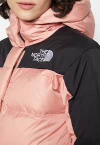 Pink and black insulated jacket with a high collar, featuring a prominent logo on the chest, smooth texture, and zip closure.