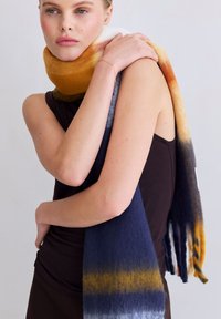 Écharpe en laine multicolore présentant un dégradé allant du jaune chaud au bleu profond, avec des extrémités à franges et une texture douce.