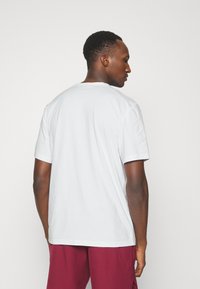 White short-sleeve t-shirt with a crew neckline, featuring a smooth texture and a relaxed fit, viewed from the back.