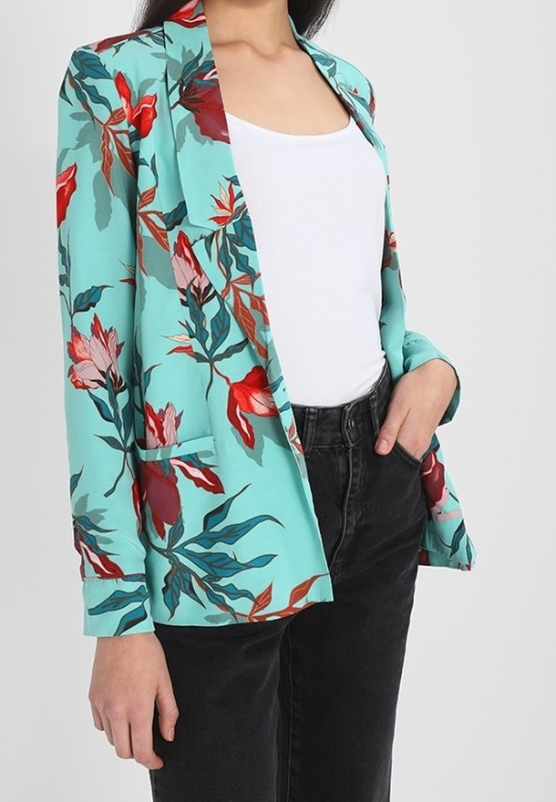 Marynarka w kwiaty w turkusowym kolorze, zdobiona czerwonymi i różowymi kwiatami, z dwiema przednimi kieszeniami i luźnym krojem, zestawiona z białą bluzką i czarnymi dżinsami.