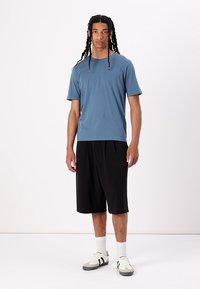 Light blue short-sleeve t-shirt paired with black knee-length shorts. Model wears white socks and grey shoes with black accents.