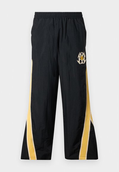 Čierne teplákové nohavice s elastickým pásom, so žltými pruhmi po bokoch a dekoračným grafickým logom na prednej strane. Ľahký materiál.