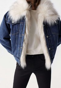 Jeansjacka med stor vit syntetisk pälskrage och innerfoder, som bärs över en ljusbeige topp och svarta byxor.