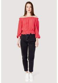 Blusa corallo scollata con scollo arricciato e maniche lunghe a sbuffo, abbinata a jeans neri a vita alta e sneaker bianche.