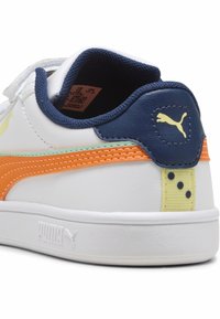 Sneaker alb cu un guler capitonat bleumarin, accente portocalii și verzi, și o tabă galbenă la toc, cu puncte albastre închise. Logo-ul Puma pe lateral.