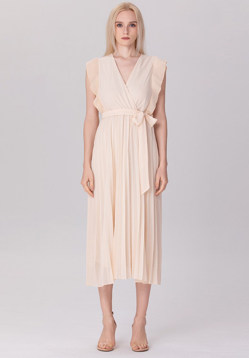Robe plissée beige clair avec des manches volantes, un col en V et une ceinture nouée à la taille, présentant un design fluide et une texture douce.