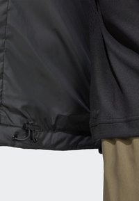 Black jacket interior featuring a smooth, shiny texture with a drawstring at the hem. The exterior edge displays ribbed fabric.