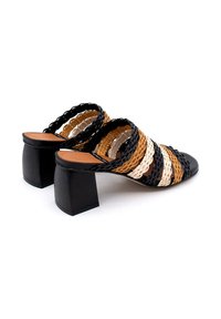 Sandalias deslizantes tejidas en negro, marrón y crema con tacón bloque grueso. Cuenta con tiras con borde en forma de ondas y una plantilla de cuero suave.