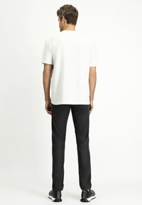 T-shirt bianco a maniche corte con colletto rotondo, abbinato a pantaloni neri e scarpe sportive. Il tessuto appare liscio e leggero.