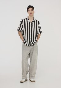 Camicia a righe bianco e nere a maniche corte, con bottoni, abbinata a jeans larghi grigi chiari e sneakers bianche con dettagli neri.