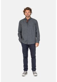 Camisa de botones gris con un acabado texturizado, combinada con pantalones oscuros y zapatillas gris. Presenta un cuello y un pequeño logo en el pecho.