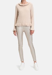 Suéter beige de canalé con un dobladillo y cuello con volantes, combinado con pantalones ajustados plateados brillantes y zapatillas de plataforma blancas.