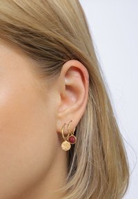 Gyldne hoops ørestikker med en tekstureret cirkulær charme og en lille rød perle, designet med en poleret finish og en sikker lås.