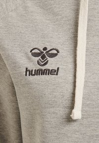 Sudadera gris con tejido texturizado, cordones en crema en contraste y un logo bordado negro con un diseño de abeja.