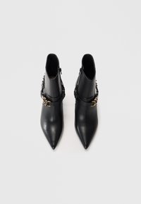 Bottines en cuir noir avec des pointes effilées, fermeture éclair et un détail décoratif en boucle et sangle dorée autour de la cheville.