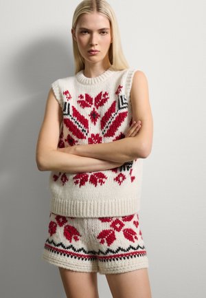 Conjunto de suéter sin mangas y pantalones cortos de punto en color crema con patrones florales rojos, acentos negros y dobladillos acanalados. Tejido de punto texturizado y grueso.