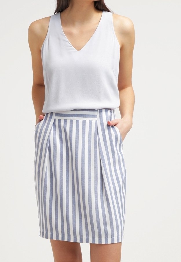 Světle šedá bezrukávová blůza s výstřihem do V, kombinovaná s sukní ke kolenům s vertikálními modro-bílými pruhy a bočními kapsami.