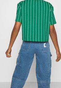 Zielona, paskowana koszulka krótki rękaw, skrócona, zestawiona z jasnoniebieskimi spodniami cargo z bocznymi kieszeniami i białą łatką z logo na tylnej kieszeni.