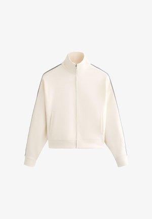 Béžová bunda na zip s vysokým límcem, dlouhými rukávy, bočními kapsami a tenkými tmavými pruhy podél ramen a rukávů.