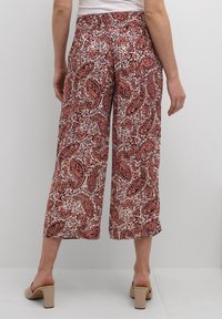 Pantalons fluides et cropped avec un motif cachemire rouge et blanc. Taille élastique et texture de tissu lisse, associés à des sandales à talons carrés.