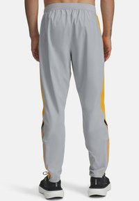 Light gray athletic pants with yellow side stripes, elastic waistband, and zippered pockets, made of smooth, lightweight fabric.