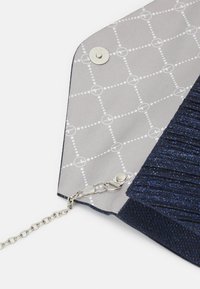 Pochette plissée bleu marine scintillante avec chaîne argentée fixée à l'intérieur, doublure intérieure grise avec un motif à grille de points blancs.