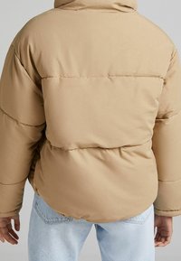 Giacca puffy beige con texture liscia, ampie cuciture orizzontali e orlo arrotondato. Abbinarla a jeans di jeans blu chiaro.