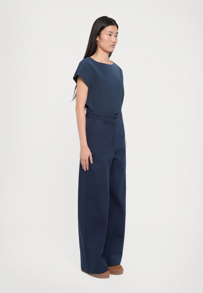 Un top bleu marin cu mânecă scurtă, asortat cu pantaloni largi cu talie înaltă, având detalii cu nasturi și pantofi cu platformă texturată de culoare maro.