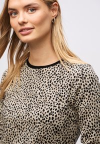 Beige neule mustalla eläinkuosilla, jossa on pyöreä pääntie ja musta reunus. Liukas pinta pitkillä hihoilla.