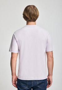 Fioletowa koszulka z krótkim rękawem, wykonana z bawełny, z okrągłym dekoltem i luźnym krojem. Brak widocznych wzorów czy grafik.