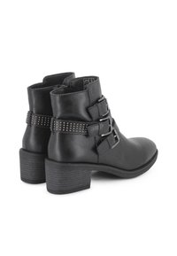 Botines negros de tobillo hechos de cuero suave, con tres hebillas plateadas y una banda decorativa con tachuelas, y un tacón apilado.