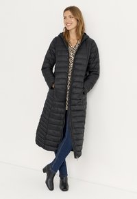 Sort puffet jakke med et langt, quiltet design, hætte, frontlynlås og sidelommer, båret over en stribet bluse og blå jeans.