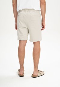 Lichtbeige shorts met een elastische tailleband, achterzakken en een gladde textuur, gecombineerd met lichtbruine instap-sandalen.