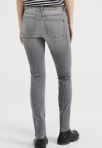 Upravené šedé džíny s hladkým povrchem, obsahující dvě zadní kapsy a charakteristický šev, spárované s černými kotníkovými botami.