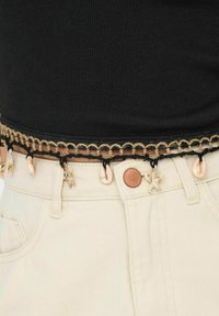 Zwart geribbeld topje met een decoratieve beige en zwarte geweven riem met schelpenaccenten, gecombineerd met lichtgekleurde denim broek.