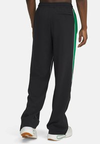 Pantalons de sport noirs avec des rayures vertes sur les côtés, une taille élastique et une poche arrière. Fabriqués en tissu léger avec une coupe décontractée.