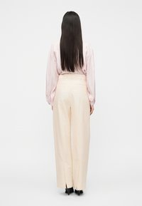 Ροζ ανοιχτό ροζ μπλούζα με μακριά μανίκια που φουσκώνουν, συνδυασμένη με εκρού παντελόνια φαρδιά με πιέτες, φορεμένα με μαύρα ψηλοτάκουνα.